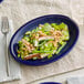 An Acopa Capri deep sea cobalt oval stoneware platter with a salad on it.