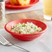 A red Acopa Capri stoneware bowl filled with food on a table with a fork.