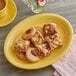 An Acopa Capri citrus yellow oval stoneware platter with pecan cookies and a cup of coffee.