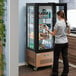 A woman standing next to a copper Avantco glass door refrigerator.