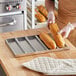 A person holding a Baker's Lane sub sandwich roll pan with a loaf of bread.