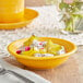 A yellow Acopa Capri stoneware fruit bowl on a table with fruit in it.