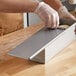 A person wearing gloves slides a metal cover onto a Baker's Mark Pullman bread pan.