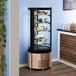 An Avantco circular glass refrigerated display case with cakes and desserts on it.