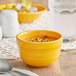 An Acopa Capri mango orange stoneware bouillon with a spoon in it on a table.