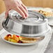An American Metalcraft stainless steel plate cover being placed over a plate of food.