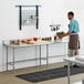 A man in a brown apron standing in a professional kitchen in front of a Regency stainless steel work table.