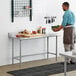 A man standing in a professional kitchen using a Regency stainless steel work table to hold a bowl of greens.