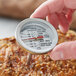 A person using a Comark EMT2K dial meat thermometer to check meat temperature.