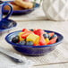 A deep sea cobalt Acopa stoneware bowl filled with fruit on a table.