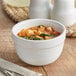 A bowl of soup with pasta and vegetables in a white Acopa Capri stoneware bouillon.