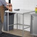 A man standing next to a Regency stainless steel open base work table.