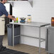 A man in a white apron standing next to a Regency stainless steel open base work table.