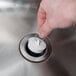 A hand holding a white rubber sink stopper over a metal drain.