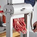 A hand holding a black and white Backyard Pro Butcher Series Jerky Slicer Blade set being used to cut meat.