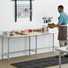 A man in a professional kitchen standing in front of a Regency stainless steel open base work table.