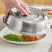 A hand using an American Metalcraft stainless steel plate cover over a plate of food.