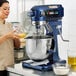 A woman using a Waring Planetary Stand Mixer with a glass bowl to mix white powder.
