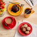 A table with red Acopa Capri stoneware cups of coffee and plates of food.