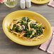 An Acopa Citrus Yellow oval stoneware platter with pasta and vegetables on it.