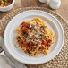 A white Acopa Capri stoneware plate with spaghetti and meat sauce and a fork.