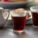 A Duralex Amalfi shot glass filled with brown liquid on a table.