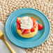 A close-up of a Caribbean turquoise Acopa Capri stoneware plate with a dessert of strawberries and whipped cream.