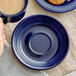 A hand holding a cup of coffee and a blue Acopa Capri saucer on a table.