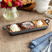 A Valor pre-seasoned cast iron tray with three compartments holding desserts on a table.