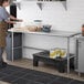 A woman in a professional kitchen using a Regency stainless steel work table.