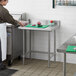 A man in a white apron standing at a Regency stainless steel work table.