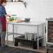 A woman in a professional kitchen using a Regency stainless steel open base work table.