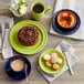 A green Acopa Capri stoneware mug filled with brown liquid on a table with plates of food and coffee.