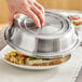 A hand using an American Metalcraft stainless steel plate cover to place over a plate of food.