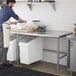 A man in an apron using a Regency stainless steel open base work table.