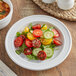 A white Acopa Capri stoneware plate with a salad of tomatoes, cucumbers, and greens.