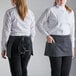 Two women wearing black and white pinstripe standard waist aprons on a kitchen counter.