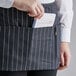 A person putting a piece of paper in a Choice black and white pinstripe apron pocket.