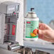 A hand holding a Rubbermaid Microburst 9000 Mango air freshener can.
