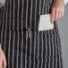 A woman wearing a black and white chalk stripe tuxedo apron holding a piece of paper and a pen.