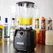 A Hamilton Beach polycarbonate blender jar filled with yellow liquid on a counter.