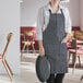 A woman wearing a Choice black and white striped bib apron holding a tray in a professional kitchen.