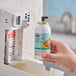 A hand holding a Rubbermaid Mango Metered Aerosol Air Freshener canister.