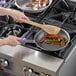 A person cooking food in a Vollrath stainless steel fry pan on a stove.