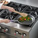 A person cooking vegetables in a Vollrath stainless steel fry pan.