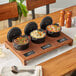 A rustic chestnut display stand with three cast iron pots of food on a wood table.