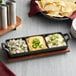 A Valor mini cast iron divided server on a wood surface with dips and chips.