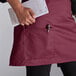 A woman wearing a burgundy half bistro apron holding a pen and paper.