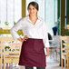A woman in a white shirt wearing a burgundy half bistro apron with 2 pockets.
