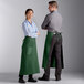 A man and woman wearing Choice hunter green bistro aprons standing in a professional kitchen.